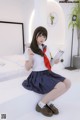 A woman in a school uniform sitting on a bed.