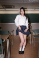 A woman in a school uniform posing in front of a blackboard.