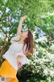 A woman in a white shirt and yellow skirt standing under a tree.