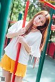 A woman in a white shirt and yellow pleated skirt posing for a picture.