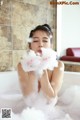 A woman in a bathtub with foam on her face.