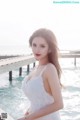 A woman in a white dress standing on a pier by the water.