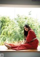 A woman in a red dress sitting on a window sill.