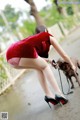 A woman in a red dress is walking a brown dog.