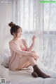 A woman sitting on a bed in front of a window.