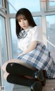 A woman in a school uniform sitting on a window sill.